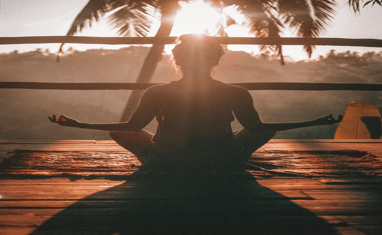 Persona meditando al atardecer frente a palmeras